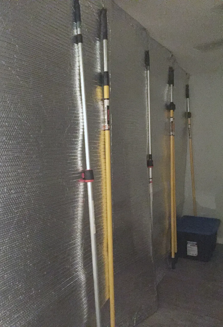 Temporary wall of reflective insulation on spring-loaded poles, splitting an open-plan living area into sections for heat treatment